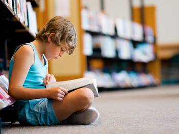 Junge liest Kinderbücher in Bibliothek