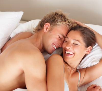 Ein Paar mit Sex-Ratgeber lacht im Bett
