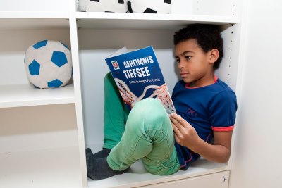 Junge liest Was ist was Buch im Schrank sitzend