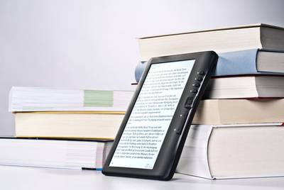 E-Reader, wie Tolino shine lehnt gegen einen Bücherstapel